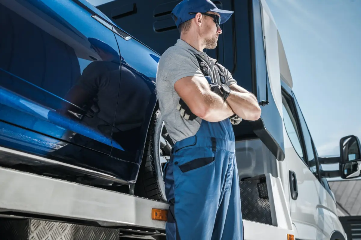 Illustration: man in work dungarees standing by a recovery truck carrying a blue car