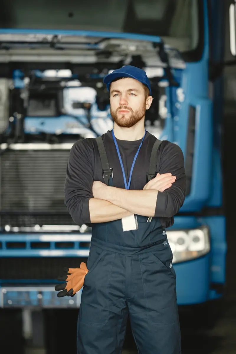 Illustration: mechanic in a blue cap and dungarees in front of a truck with its front grille open