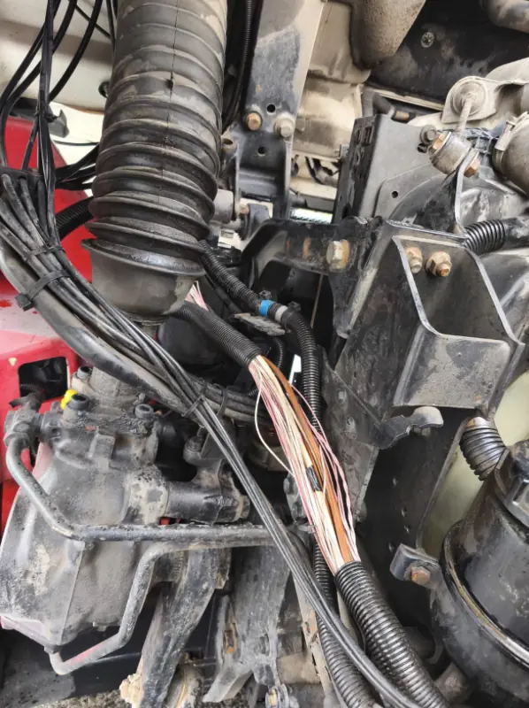 Electrical wiring harnesses and the air intake hose in the engine bay of a red truck