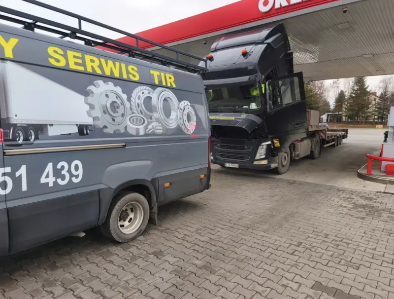 Mobile service van at a petrol station beside a black Volvo with its cab tilted and a low-loader trailer