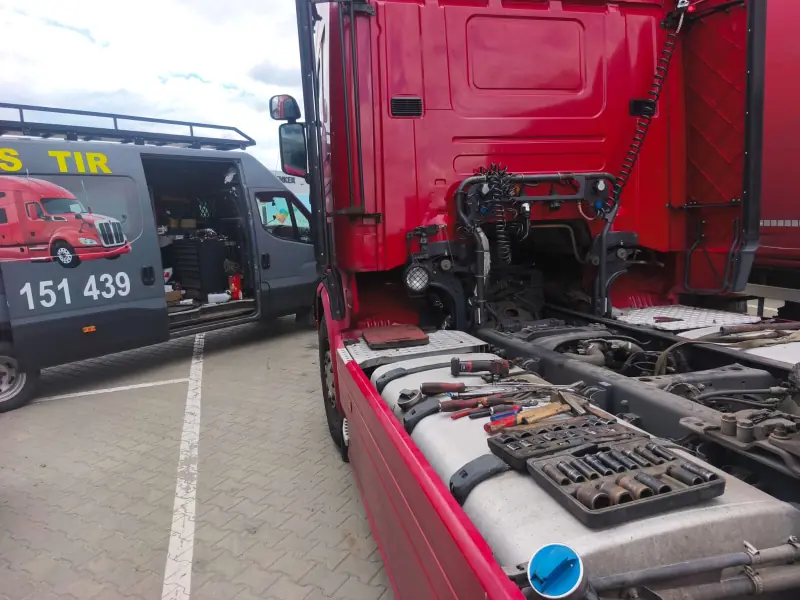 Tools laid out on the tank of a red tractor unit with its cab tilted, service van alongside