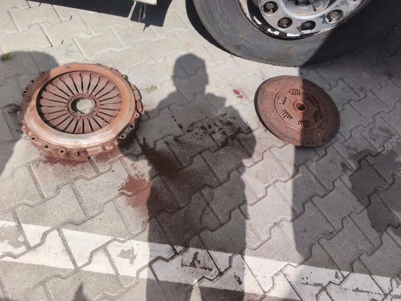 Worn clutch pressure plate and clutch disc lying on paving next to a truck wheel