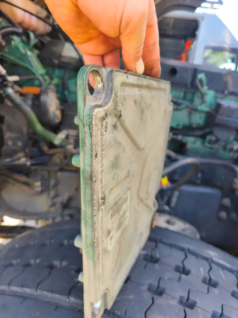 Mechanic holding the removed ECU in front of a green truck engine