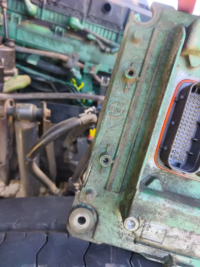 Engine ECU with a cracked mounting lug next to a green Volvo engine