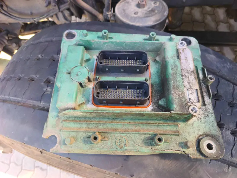Removed engine ECU with two harness connectors, resting on a truck tyre